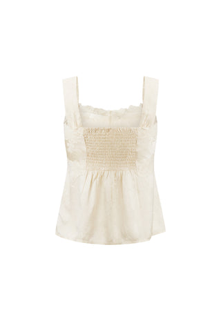 an-off-white-sleeveless-smocked-top-with-wide-shoulder-straps-and-a-ruffled-neckline-shown-against-a-plain-white-background
