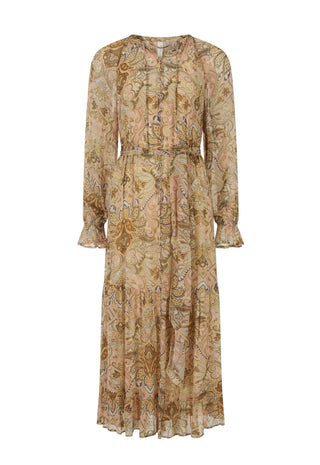 A woman outdoors in a grassy park wearing a flowing sheer boho-style maxi dress with an intricate paisley and floral pattern in warm beige